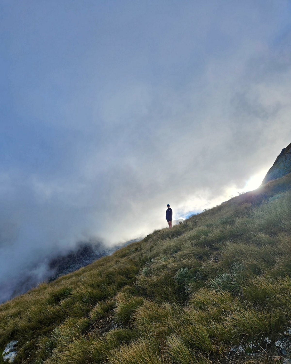 A runner on a grassy mountain ridge surrounded by cloud